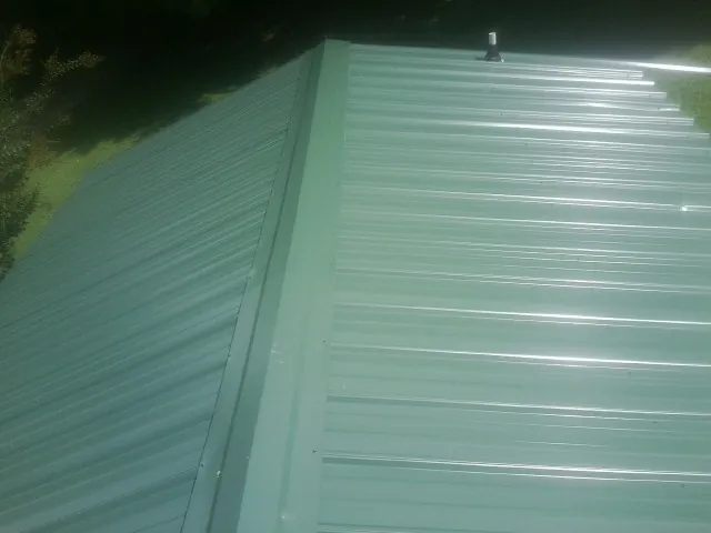 New green metal panels meeting at the ridge of a roof — Flat Roof Repair work by our crew in Cross Plains