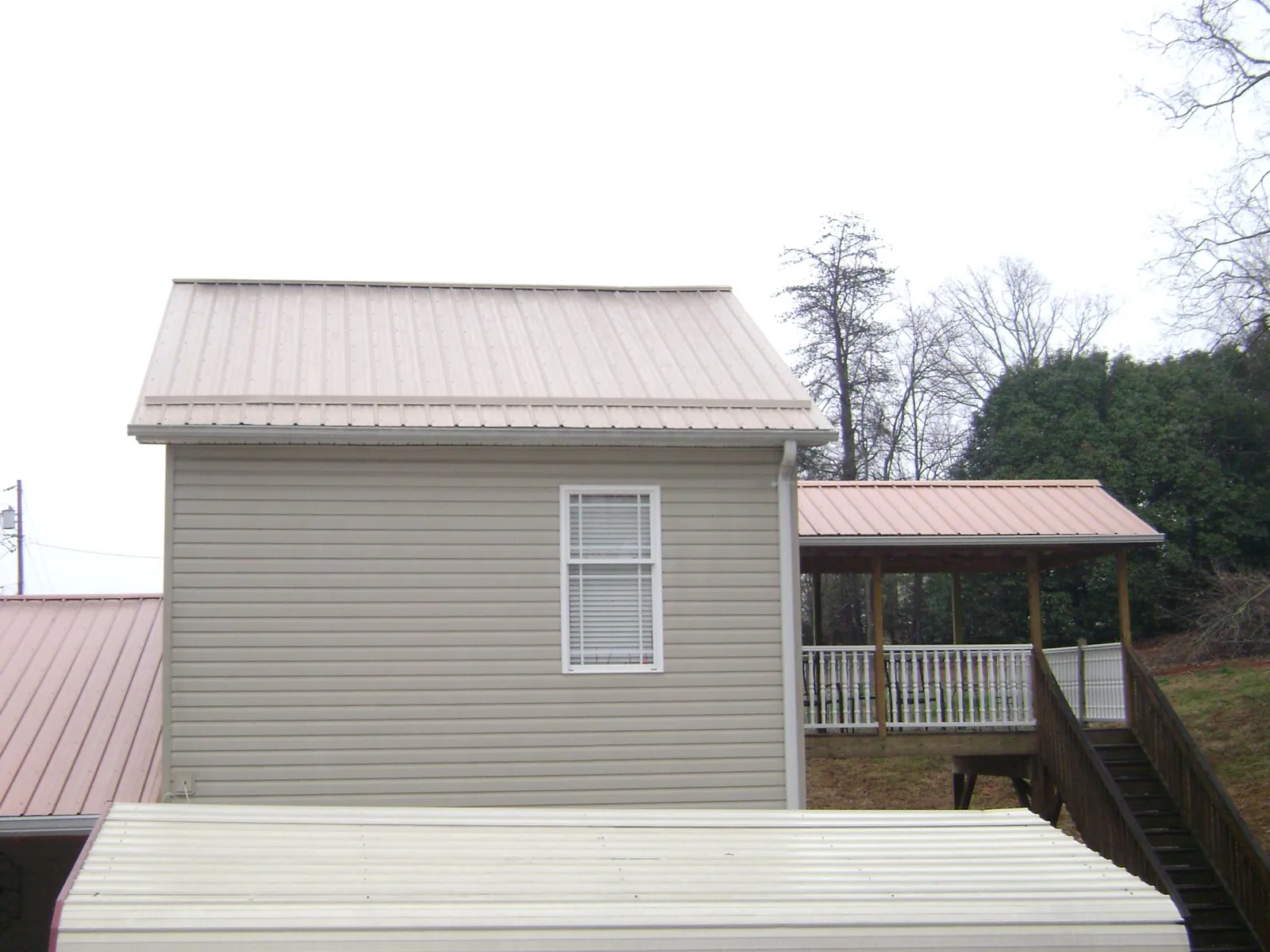 Tan metal roofs on a two story addition and attached porch, from a Roof Replacement job in Cross Plains